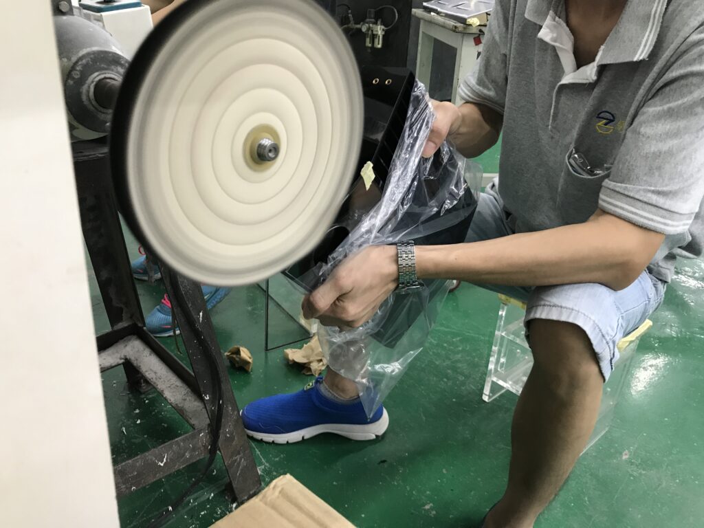 Factory worker polishing retail display rack with rotary buff wheel to fix uneven surface and smooth rough edges in Dongguan workshop